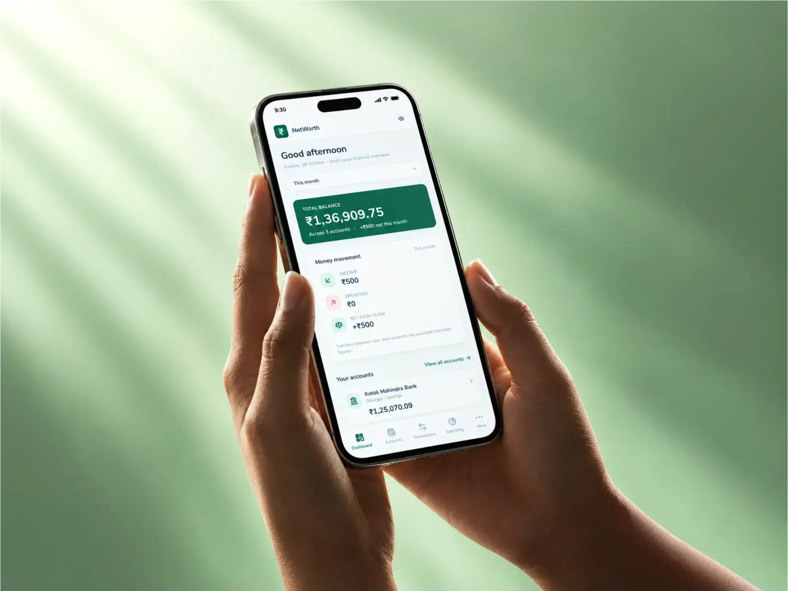 A phone held in both hands showing Networth's dashboard: the total balance across three accounts, and the month's income, spending and net cash flow under it